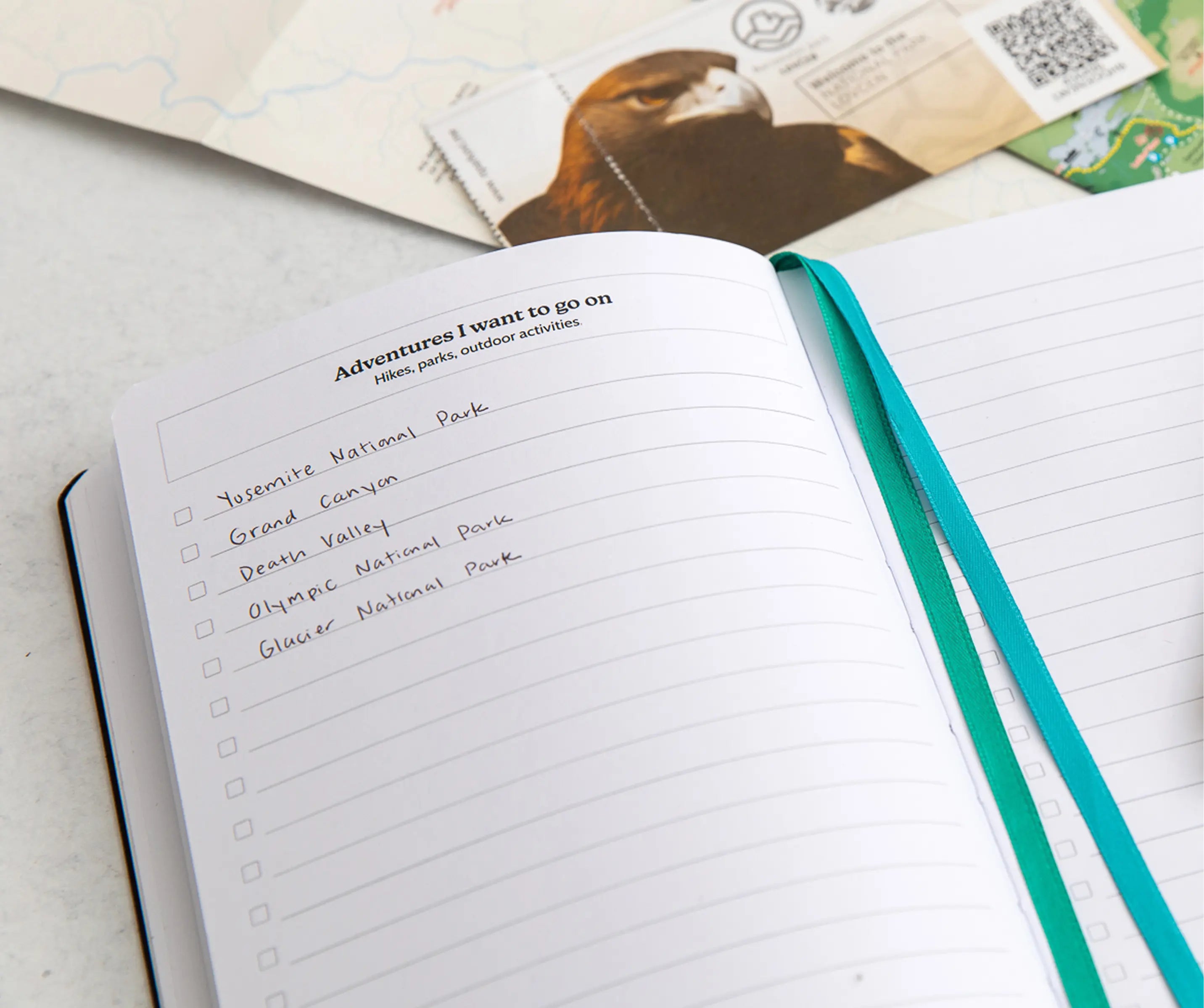 Open travel journal with a list of adventures I want to go on including several national parks on a light surface