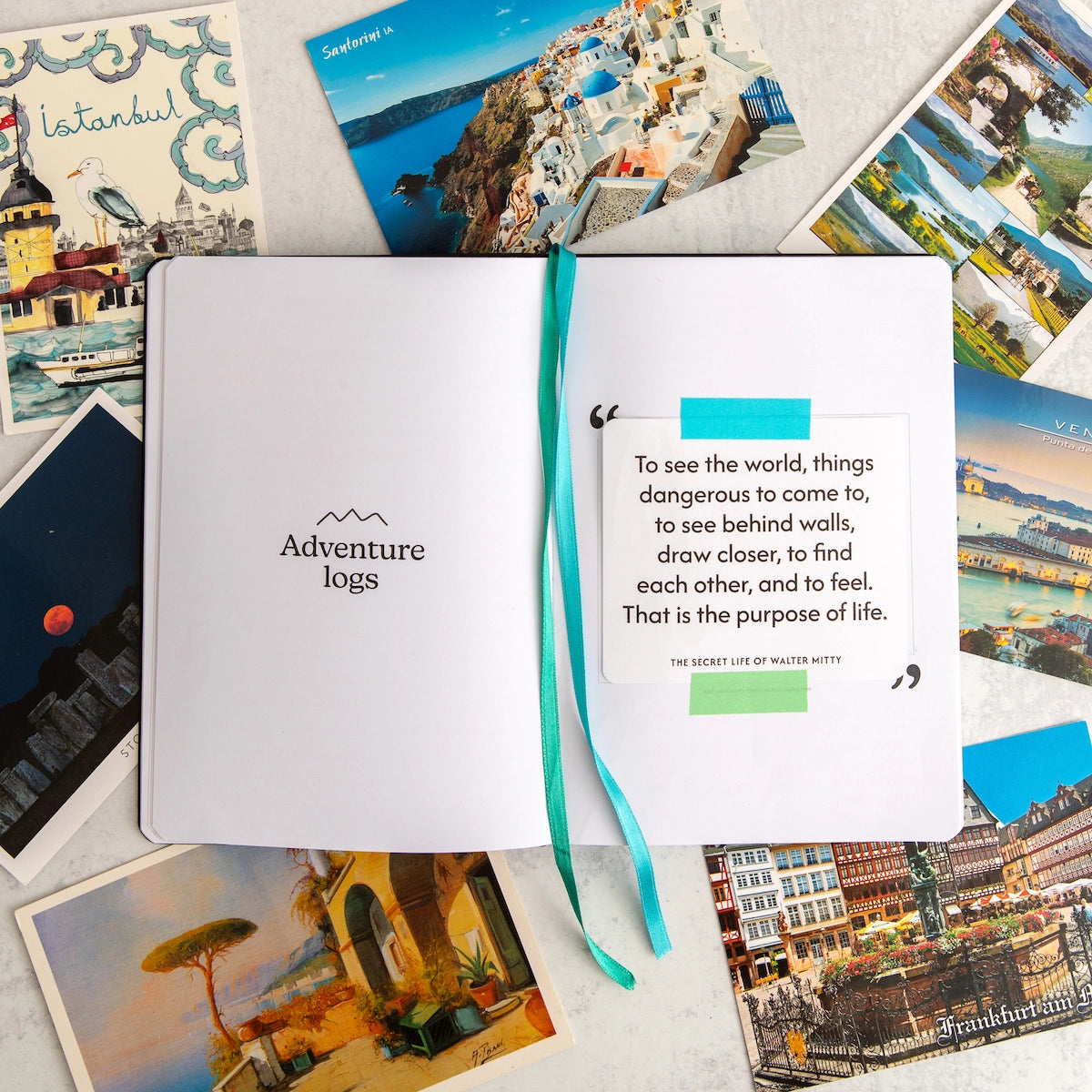 Open travel journal with Walter Mitty quote and travel-themed postcards on a light surface